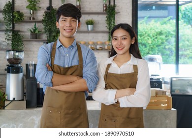 Asian couple Barista or owner small business in apron looking at camera ready to give Coffee Service at the modern coffee shop