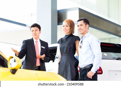 Asian Couple Buying Car In Auto Dealership Consulting The Salesman 