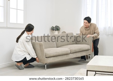 Asian couple carrying sofa while rearranging living room