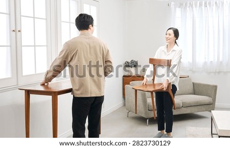 Asian couple carrying table while rearranging living room