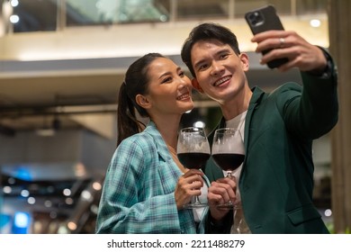 Asian Couple Celebrating Holiday Event At Luxury Restaurant At Night. Man And Woman Couple Using Mobile Phone Taking Selfie Together While Having Dinner And Drinking Wine At Bar On Summer Vacation