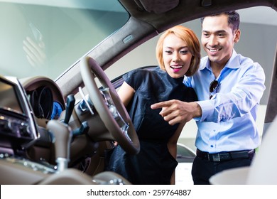Asian Couple Choosing Luxury Car In Auto Dealership Looking At The Interior