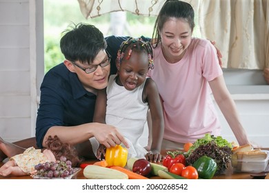 Asian Couple Cooking And Tasting Food With African American Girl Together In Kitchen At  Home . 