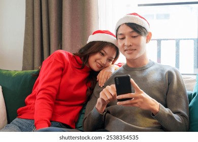 Asian couple in cozy Christmas attire, woman leaning affectionately on partner's shoulder while both look at a phone. Peaceful, intimate moment reflects holiday festive home environment. - Powered by Shutterstock