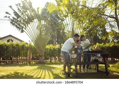 Asian couple with daughter gardening while watching laptop together in the backyard garden. Happy family gardening together and taking care of nature. People and ecology concept.