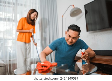 asian couple doing domestic chores together, wiping table and mopping the floor