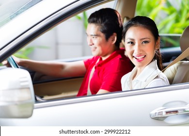 Asian Couple Driving New Car On Driveway To Their Home