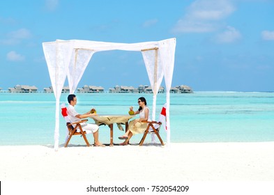 Asian Couple Enjoying Romantic Luxury Lunch Setting At Tropical Beach In Maldives