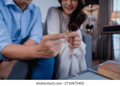Asian couple experiencing relationship problems and considering divorce or separation, showing frustration while holding their wedding rings, symbolizing marital issues and the end of commitment