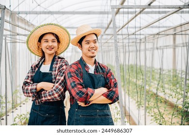 Asian couple farmers thrive in tomato hydroponic farm. Smiling husband and wife crossed arms carrying quality vegetables. Portrait of success in the greenhouse. Farming happiness. - Powered by Shutterstock