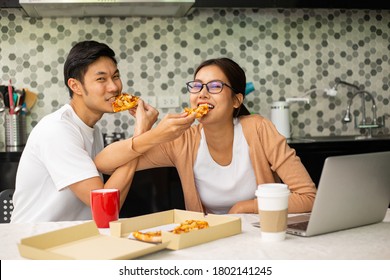 Asian Couple Funny With Their Pizza Food.Two Thai People Have Lunch In The Kitchen Room.Take Away Food.Cross Arm For Eat Food.