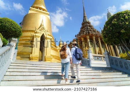 Asian couple happy tourists to travel wearing mask to protect from Covid-19 on they holidays in Wat Phra Kaew Temple in Bangkok, Thailand