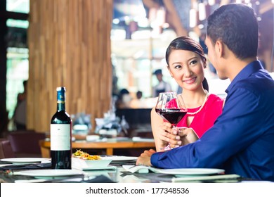 Asian Couple Having Dinner And Drinking Red Wine In Very Fancy Restaurant With Open Kitchen In Background