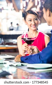 Asian Couple Having Dinner And Drinking Red Wine In Very Fancy Restaurant With Open Kitchen In Background