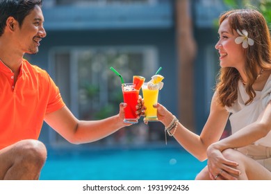 Asian Couple Having Goodtime Together Sitting By Resort And Hotel Pool With Glass Of Fruit Juice Water Melon And Pineapple Juice On Hand During Summer Vacation