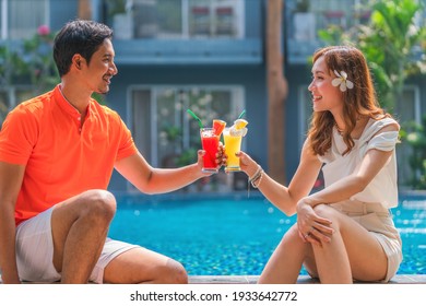 Asian Couple Having Goodtime Together Sitting By Resort And Hotel Pool With Glass Of Fruit Juice Water Melon And Pineapple Juice On Hand During Summer Vacation