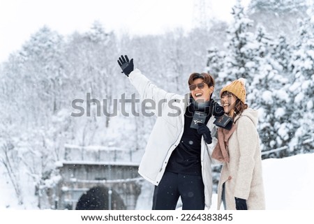 Asian couple holding passport during travel small village and forest mountain covered in snow together in snowy day. Global airline transportation and people travel Japan on winter holiday vacation.