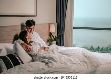 Asian couple is hugging and smiling sitting on the bed in a bedroom evening.Couple in Valentine day.Love couple,Relationship and couple concept.