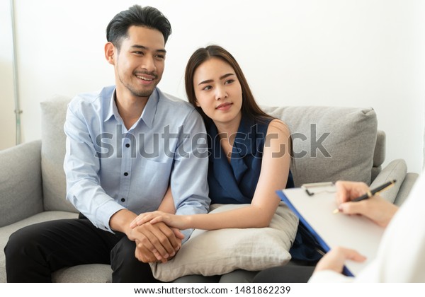 Asian couple join hand to\
encourage while sitting on the couch in the psychiatrist room to\
consult mental health problems by doctor, Health and illness\
concepts