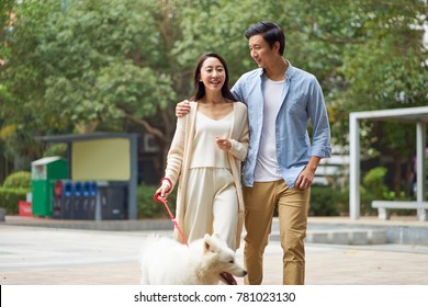 Asian Couple Laughing While Walking Dog Outdoor In Garden