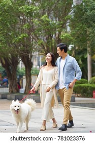 Asian Couple Laughing While Walking Dog Outdoor In Garden