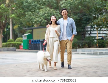 Asian Couple Laughing While Walking Dog Outdoor In Garden