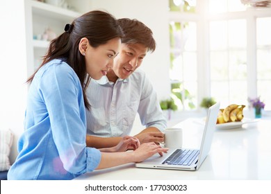 Asian Couple Looking At Laptop In Kitchen