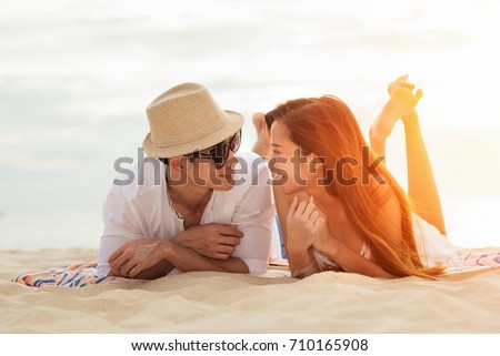 Asian couple lying Honeymoon at sunset tropical beach in Thailand