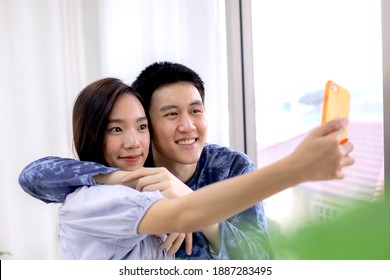 Asian Couple Making A Selfie At Hotel Room By Smartphone. Asian Couples Taking Selfies At Resort Room. Journey, Travel Concept. Honeymoon Trip