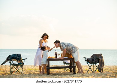 Asian couple man and woman with little daughter enjoy dinner party together on island beach at summer sunset. Happy family parents with cute child girl relax and having fun with on holiday vacation - Powered by Shutterstock