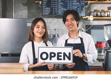 Asian Couple owner barista cafe holding Open sign to welcome customer standing at counter in coffee shop. - Powered by Shutterstock