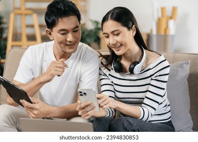 Asian couple relaxing with smartphone at home, loving man and woman sitting on couch together, Browsing Internet on mobile phone and laptop. - Powered by Shutterstock