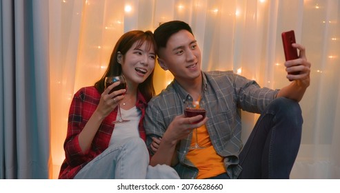 Asian Couple Sitting On Floor Take Selfie With Red Wine While Celebrating Anniversary In The Night Living Room At Home