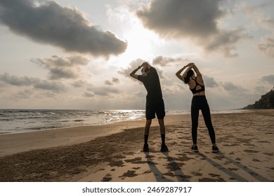 Asian Couple stretching arms and legs before running outdoors sea sand beach. Sporty people warm up body before jogging. Athlete running during sunset on the beach. Workout exercise. - Powered by Shutterstock