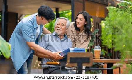 Asian couple surprised elderly father with Birthday gift at outdoor cafe restaurant on summer holiday vacation. Family relationship, celebrating father's day and older people health care concept.