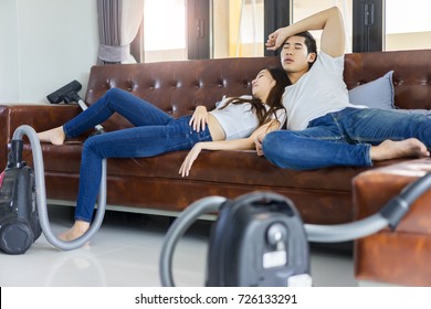 Asian Couple Tired To Cleaning Floor With Vaccuum Cleaner Sleep On A Brown Sofa At Home.