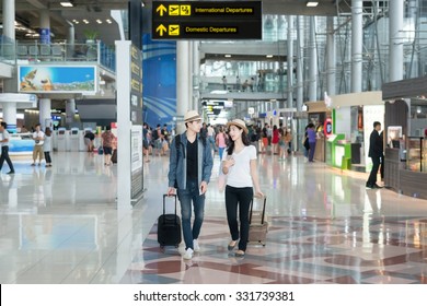 Asian Couple Traveler With Wheel Luggage At The International Airport.