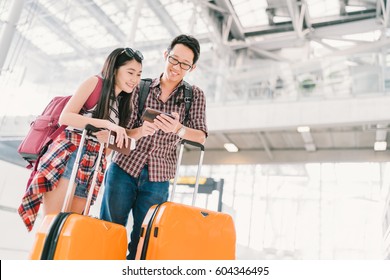 Asian Couple Travelers Using Smartphone Checking Flight Or Online Check-in At Airport, With Passport And Luggage. Air Travel Or Mobile Phone Technology Concept.