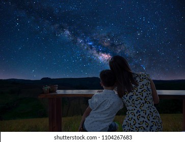 Asian Couple Traveling With Silhouette Mother And Child  Sitting On Mountain View On Green Grass. Watching Stars In The Sky And The Milky Way Happily On The Romantic Night.