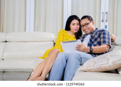 Asian couple using a digital tablet while sitting together on the couch. Shot at home