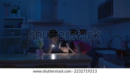asian couple using flashlight to illuminate are looking for something after power outage in kitchen at home