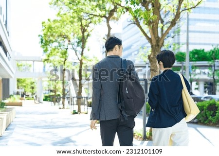 An Asian couple is walking along a stylish street surrounded by fresh greenery.