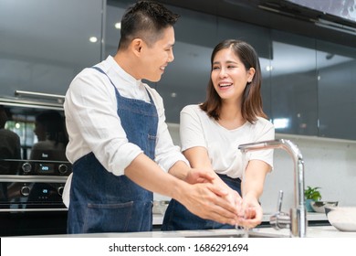 Asian couple washing hands with foam soap before cooking together. Happy smiling Young Man and woman cleaning and rubbing nails, fingers with water at sink in kitchen. Hygiene, preventing coronavirus.