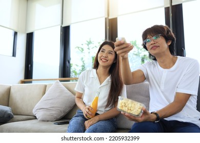 An Asian Couple Is Watching A Movie Together In The Living Room Of Their Home And Are Using The Remote Control To Turn The Volume Up Or Change Channels.