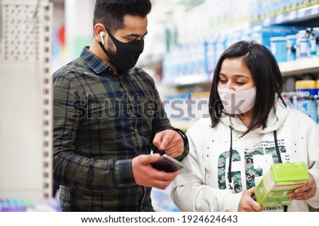 Asian couple wear in protective face mask shopping together in supermarket during pandemic. Online buying on smartphone is better choice.
