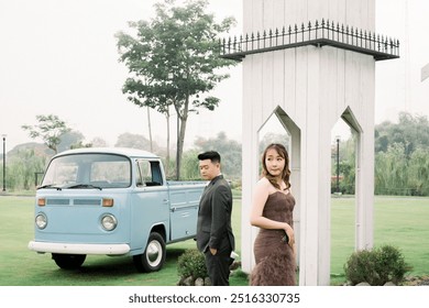 Asian couple wearing dark grey suit and brown dress at the park with blue vintage car combi van - Powered by Shutterstock