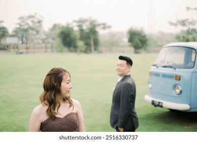 Asian couple wearing dark grey suit and brown dress at the park with blue vintage car combi van - Powered by Shutterstock