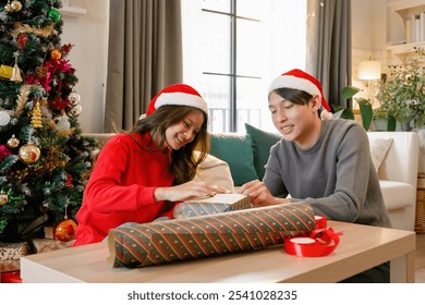 Asian couple wearing Santa hats wrapping Christmas gifts together on a table. Surrounded by festive decorations and rolls of wrapping paper, enjoying a warm holiday bonding activity in a cozy setting. - Powered by Shutterstock