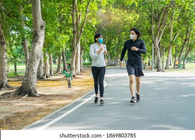 Asian Couple Wears A Covid 19 Protective Mask And Jogs In The Garden In The Morning.Health, Sports And New Normal Concept.