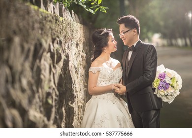 Asian Couple Wedding Outdoor Style, Bride Leans Against Stone Brick Wall